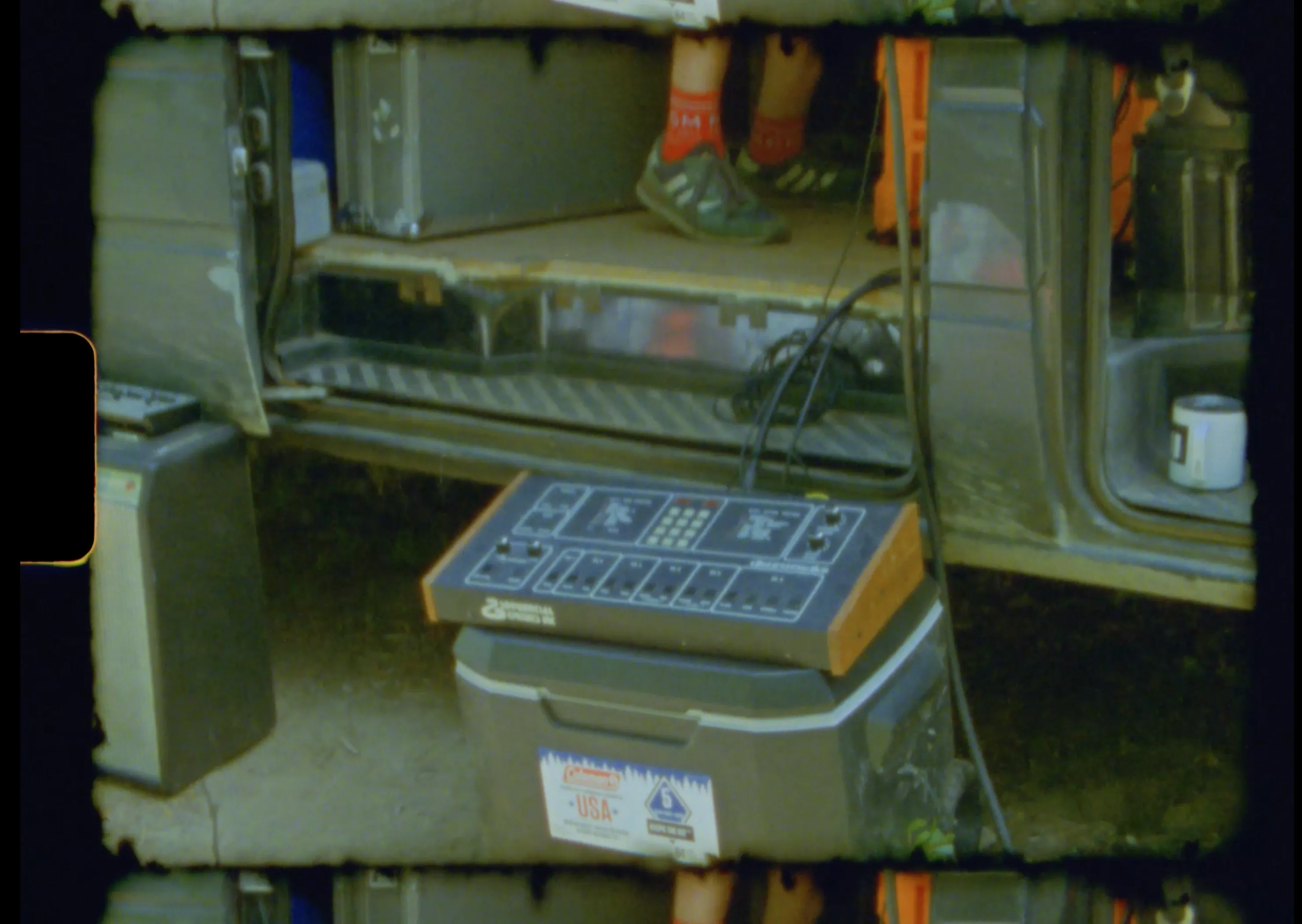 A drum machine rests on a cooler at the open door of the van, gear cases stacked inside
